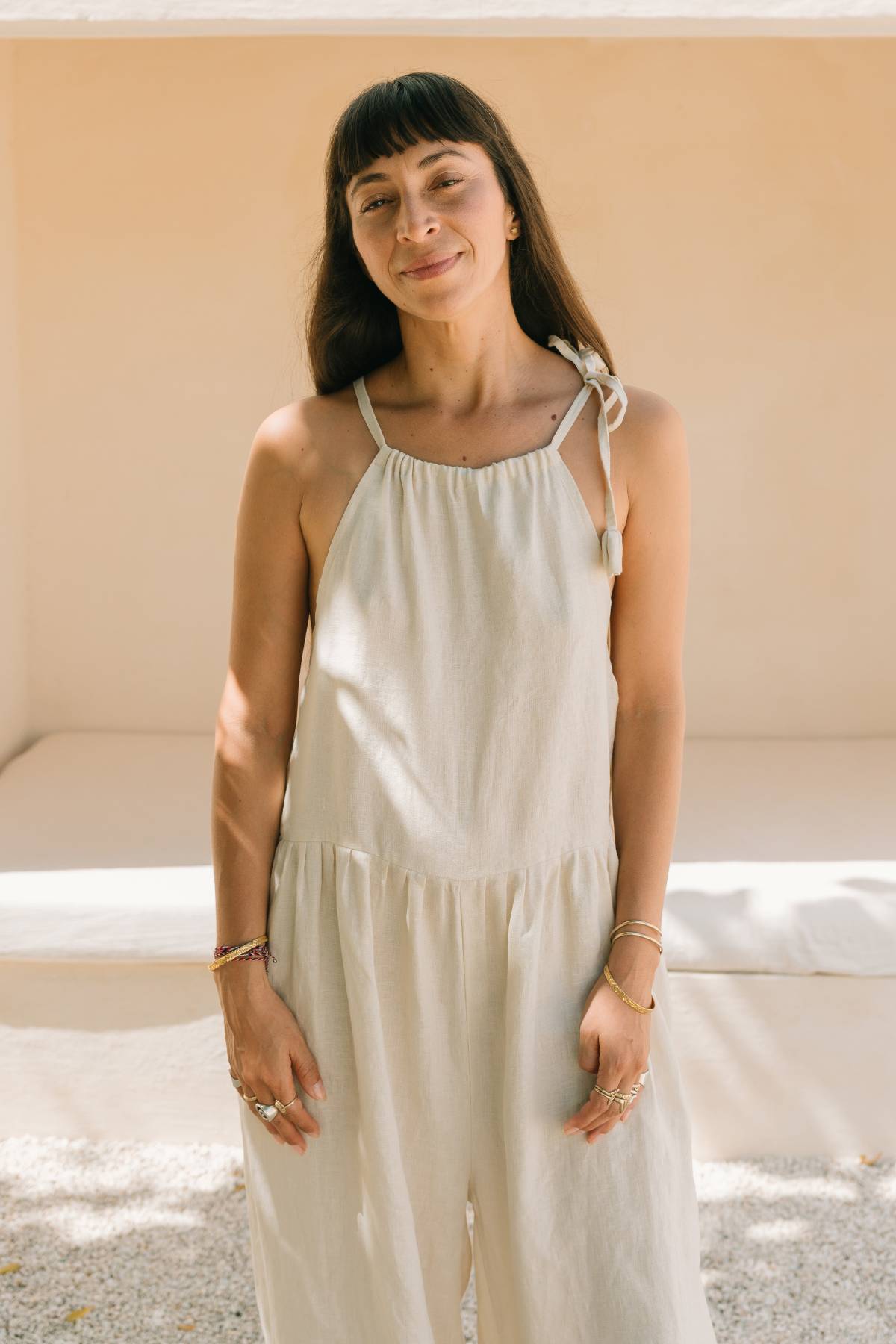 Close front view, smiling, of a woman wearing the Monaya Playsuit by Myrah Penaloza in Moonlight stone washed linen. Handcrafted in Bali.