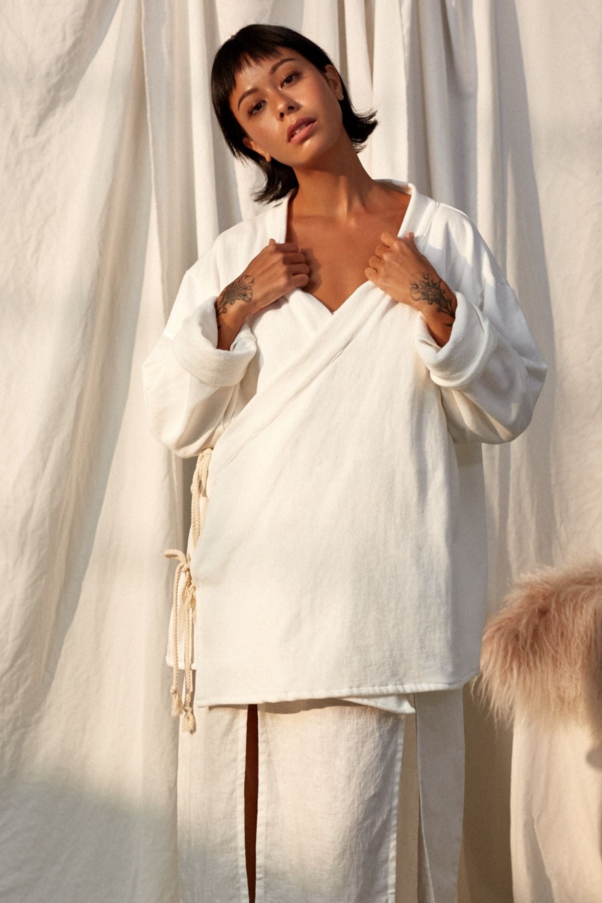 Seated view of the Chai Ba Cotton Wrap Jacket by Myrah Penaloza in cotton, handcrafted in Bali by artisan families.