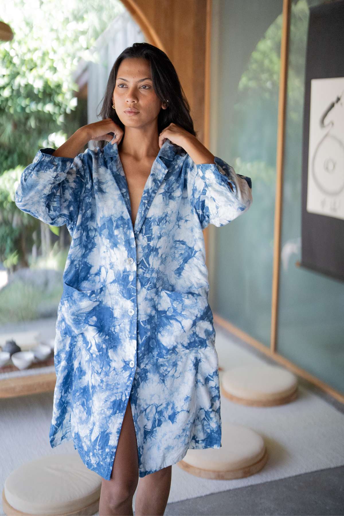 A person stands indoors wearing the Rubi Linen Jacket Indigo by Myrah Penaloza, specifically available during Black Friday. They gaze into the distance against a backdrop of wooden decor and natural light.