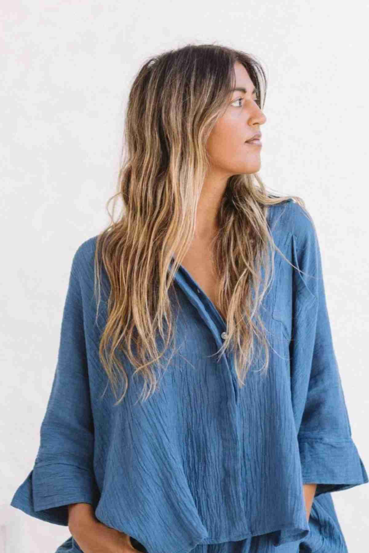 A person with long wavy hair is wearing the Suka Button Down Top Only by Myrah Penaloza, looking off to the side against a plain white background.