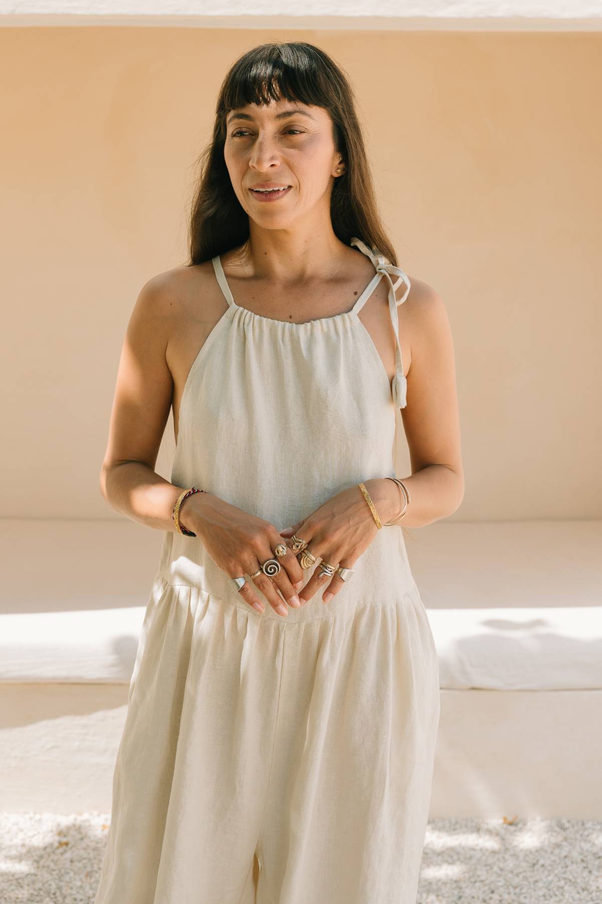 Front view of a woman standing in the Monaya Playsuit by Myrah Penaloza in Moonlight stone washed linen. Oversized, full length silhouette with tie shoulder straps and a relaxed wide leg. Handcrafted in Bali.